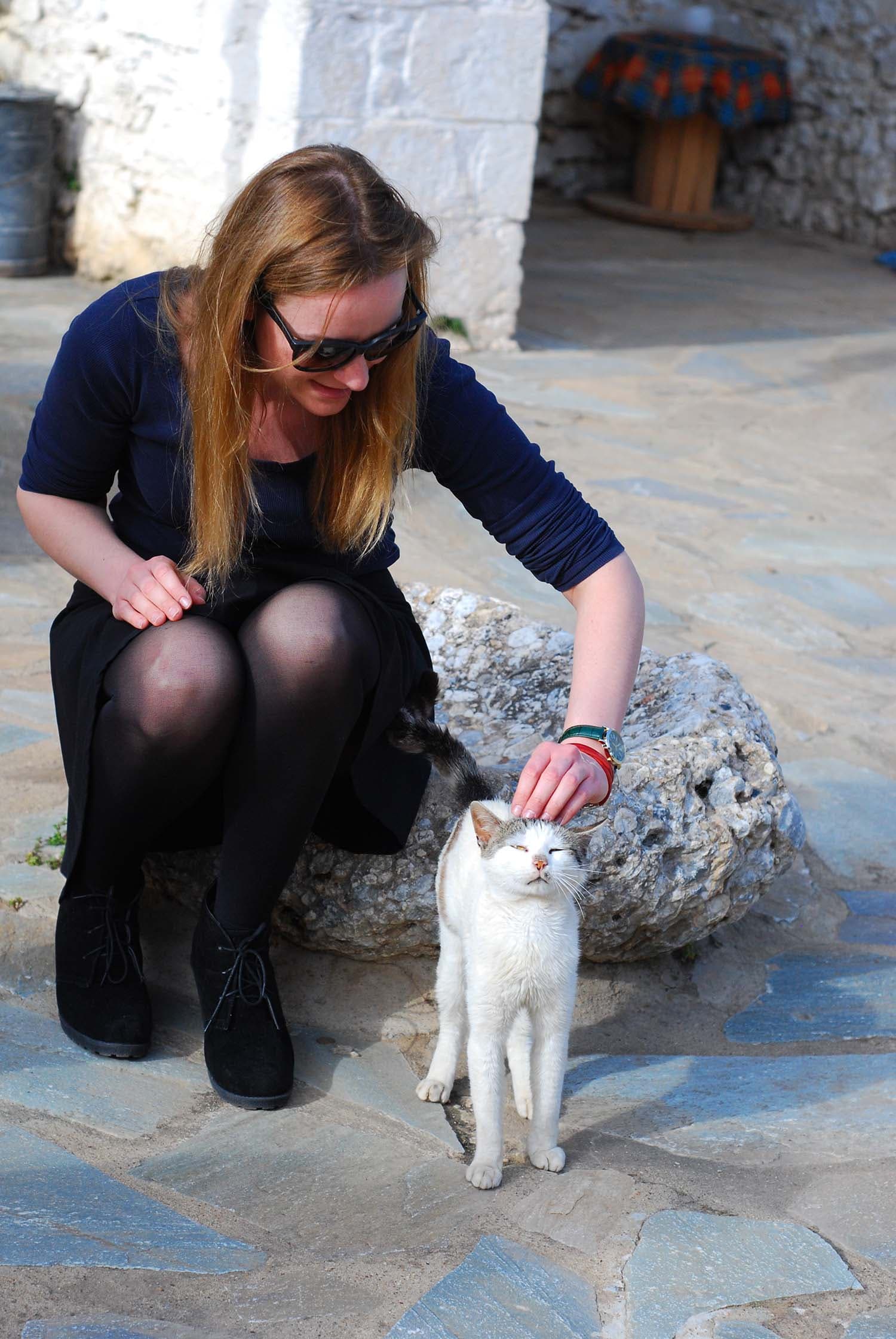 Donna accovacciata che accarezza un gatto bianco su un sentiero di pietra