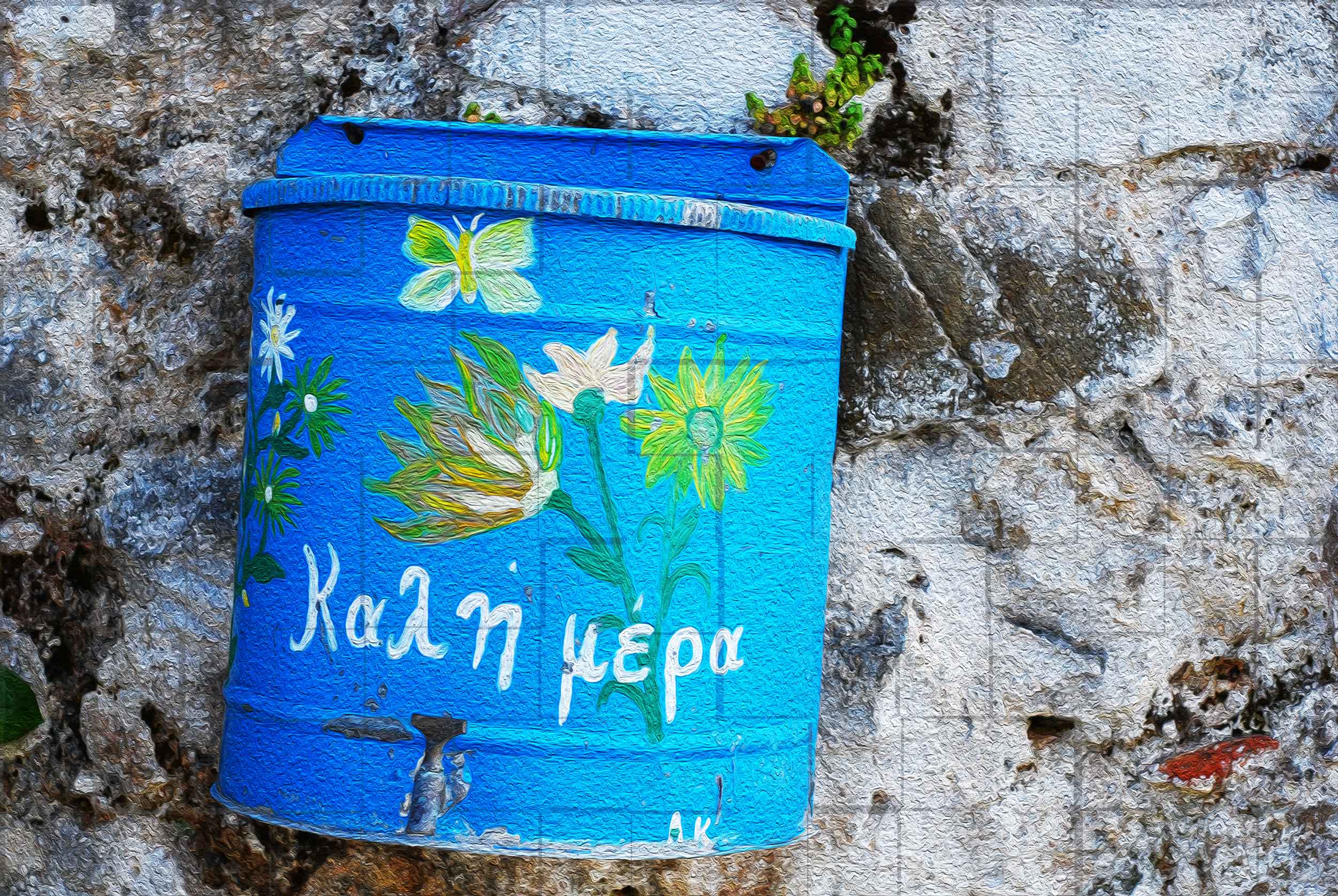 Barattolo dipinto di blu con la scritta Καλή μέρα (buongiorno) su un muro di pietra