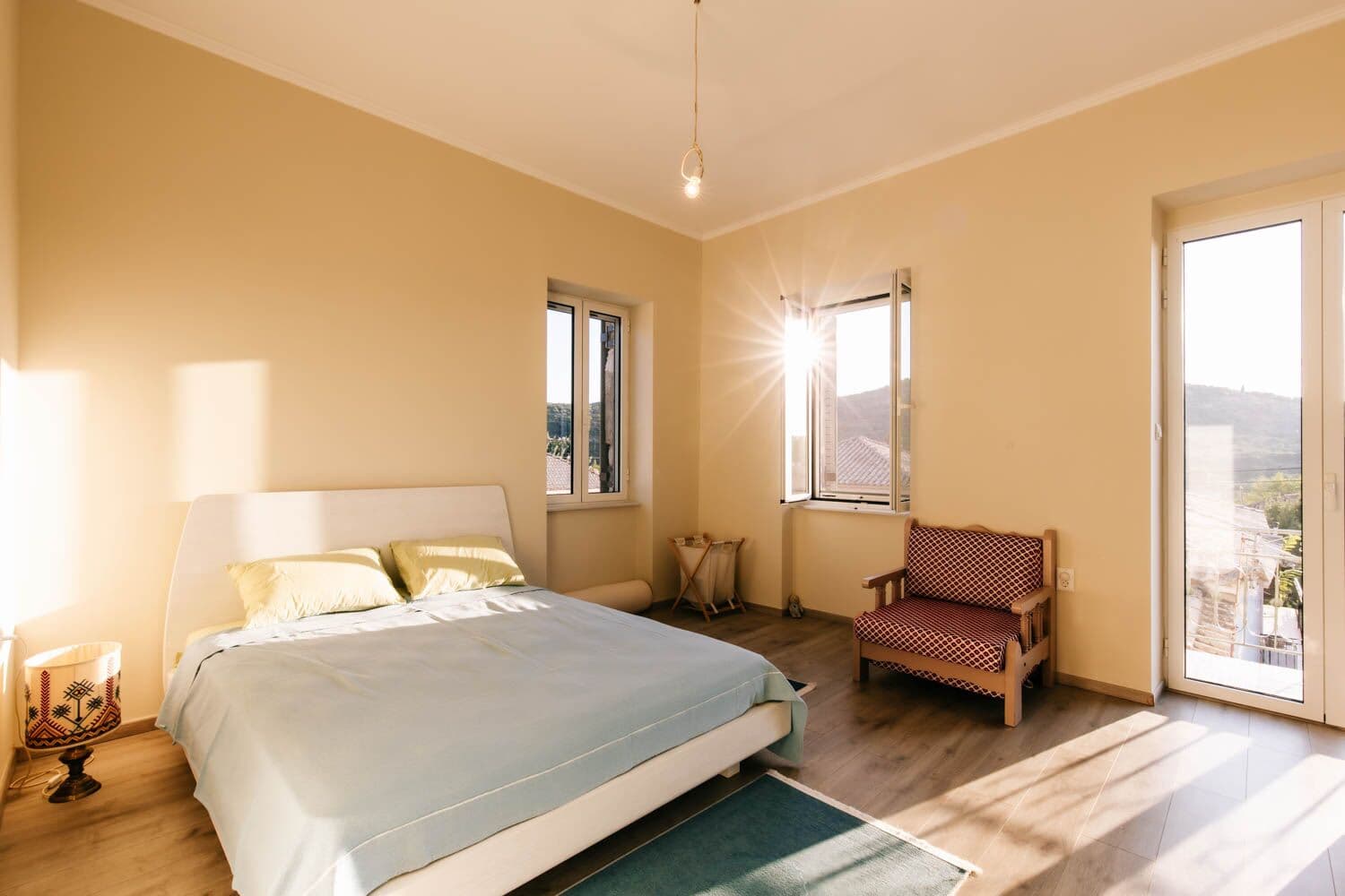 Dormitorio luminoso con una cama grande, un sillón y ventanas soleadas