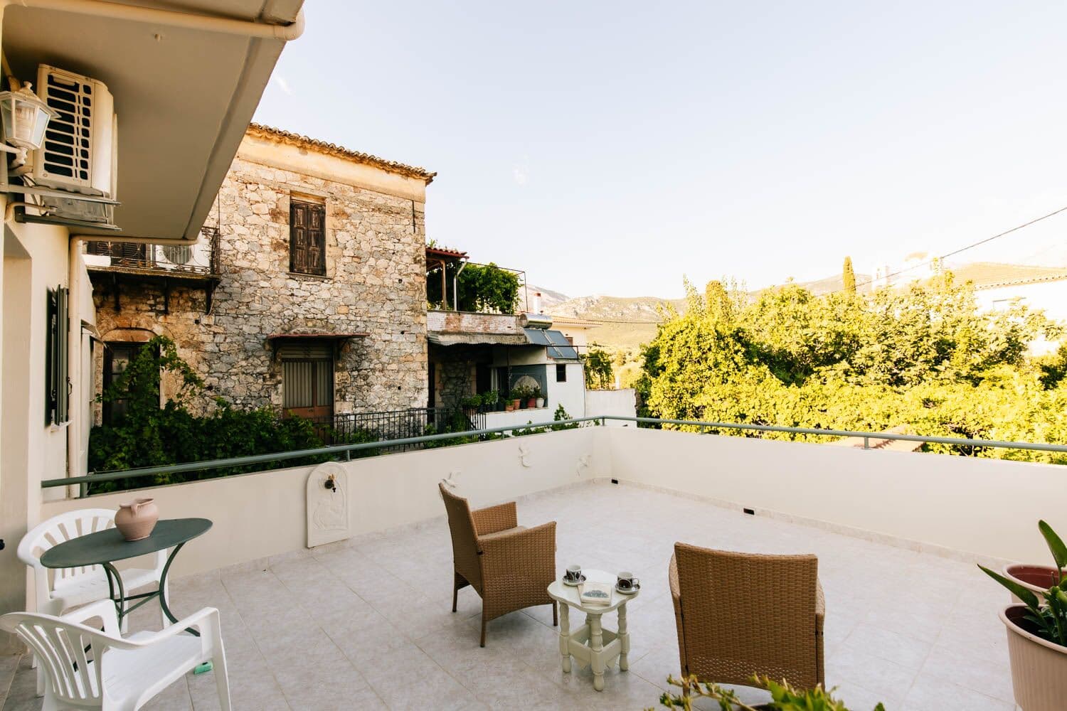 Pequeño rincón de la terraza con sillones de mimbre y una mesa frente a la casa de piedra vecina